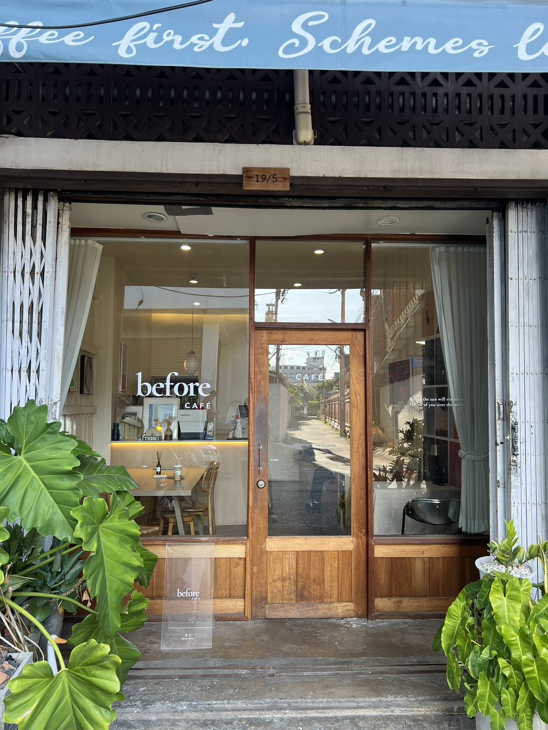 Shopfront of Before Café — wooden doorway with the brand wordmark, framed by green plants