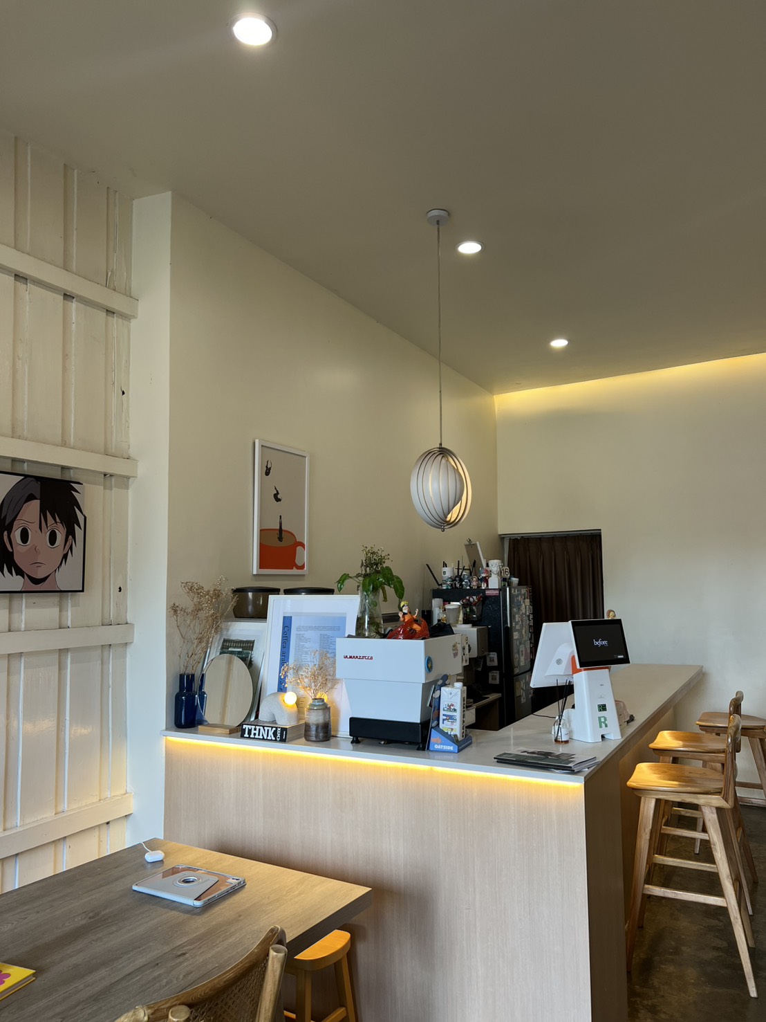 Wide view of the café — bar counter with espresso machine, wooden stools, and warm lighting